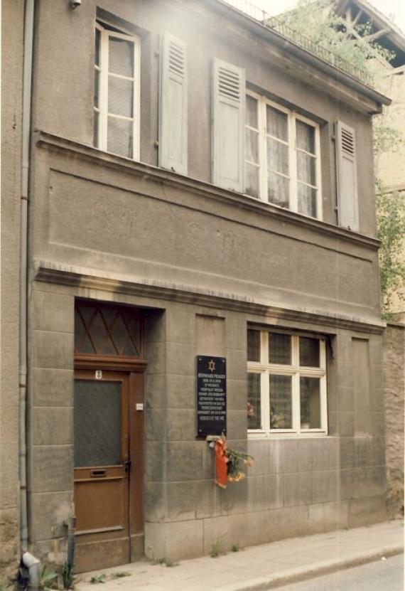 Photo in sepia, street view of the two-story house with the plaque to the right of the entrance door