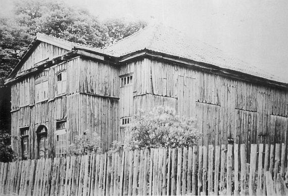 Schwarz-Weiß-Foto der mit Holz verkleideten Synagoge, die heruntergekommen wirkt