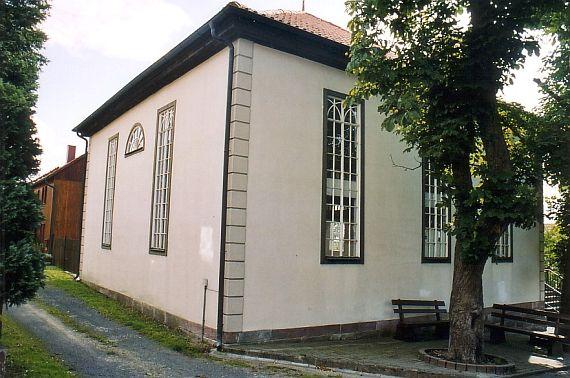 weiß verputzte Wände, davor ein Baum, der vom Pflaster umringt ist