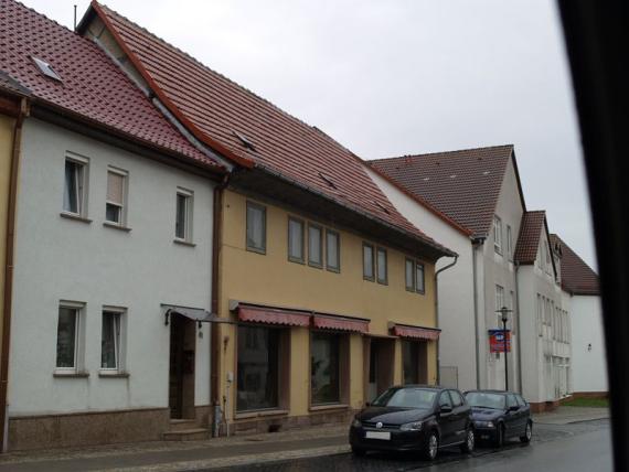 gelb verputztes Haus mit zwei Etagen, zur Straße hin Schaufenster, aber ohne sichtbares Geschäft