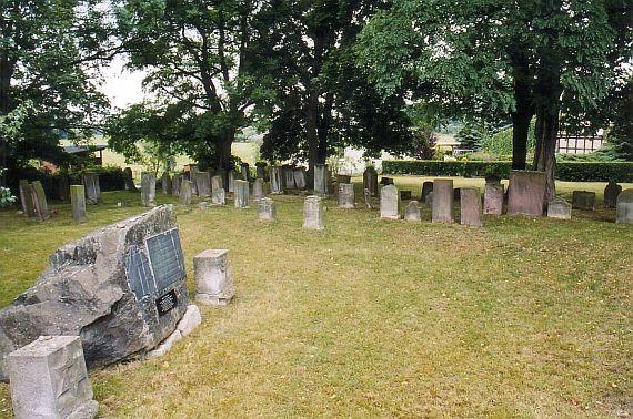 old gravestones in the background, synagogue memorial: roughly hewn rock with plaque on it