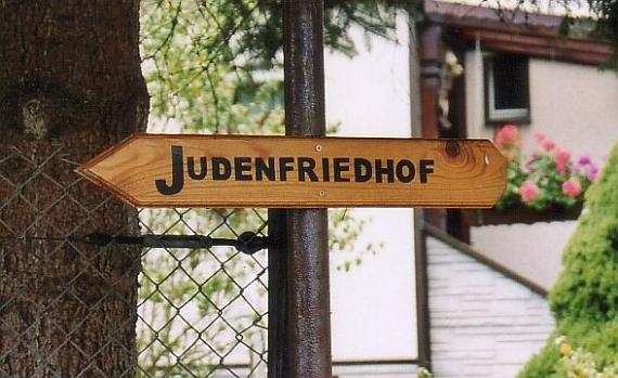 The arrow-shaped wooden sign reads "Jewish Cemetery".