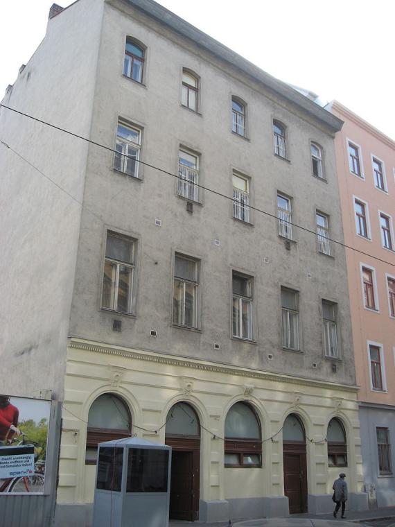 The facade of the second floor is renovated and painted yellow. The three floors above are plastered gray.