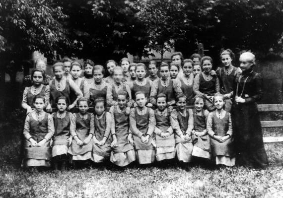 black and white group photo of uniformed girls, adult women next to them