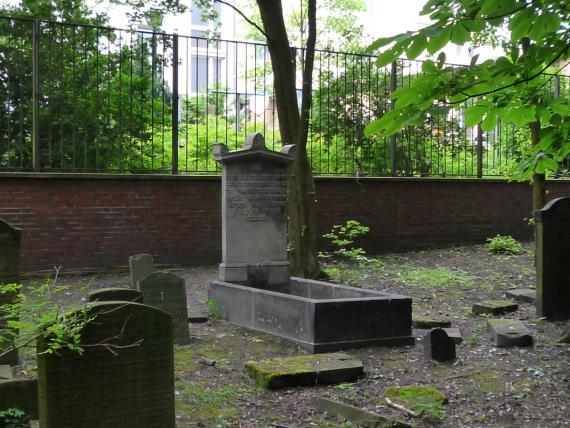 The narrow tombstone with Hebrew inscription stands in front of a grave set in stone.