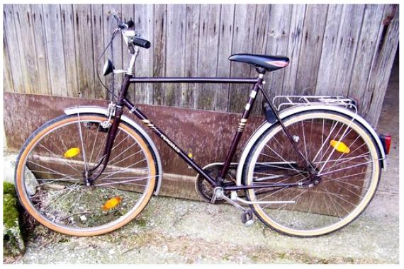 Brown bicycle leaning against wooden wall