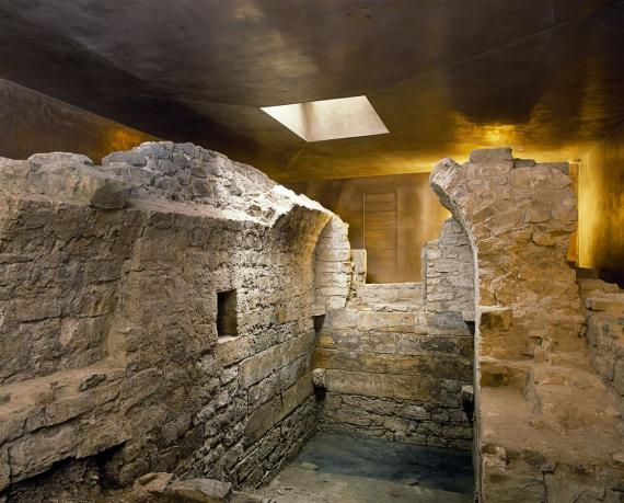 Ruins in bronze colored narrow room; walls lead into collapsed arch