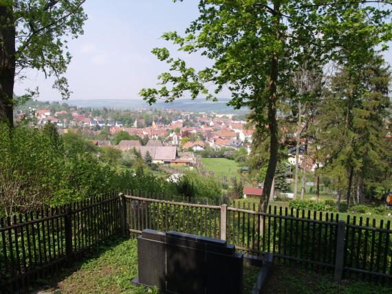 in the foreground a gravestone, behind it the wooden fence, down the hill lies the village