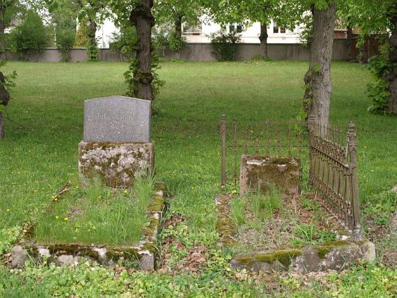 Grabstein auf hohem Sockel, Grab in Steine eingefasst; rechts daneben Grab mit Einfassungsgitter