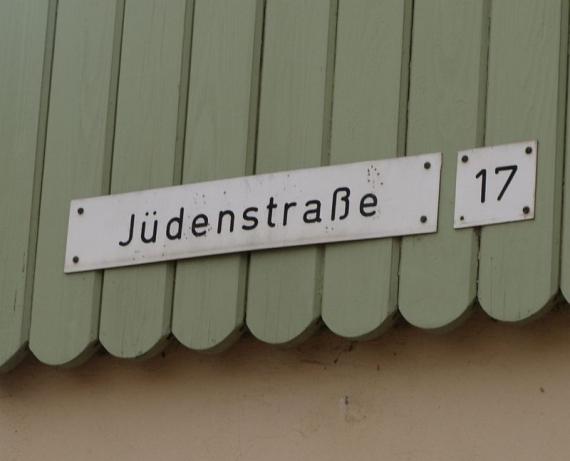 weißes Straßenschild mit Hausnummer 17 daneben, auf grüner Holzvertäfelung