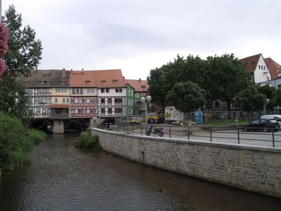 mit Häusern bebaute Brücke über einem Kanal, rechts hinter Bäumen die erwähnten Gebäude