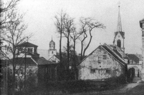 Black and white photo: on the left behind trees the synagogue with octagonal structure, on the right a church with bell tower