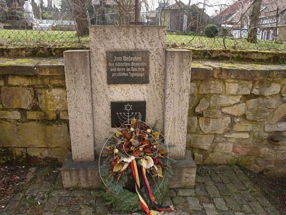 Ein Kranz mit einem Trockenblumengesteck liegt vor dem Stein