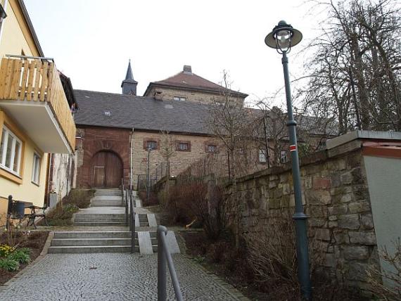 Stairs leading to a wooden gate, on the left a yellow residential house, on the right a wall