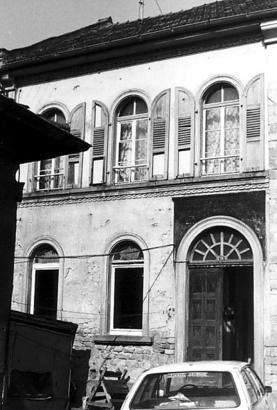 Schwarz-weiß Foto einer heruntergekommenen Hausfassade, die Tür steht offen, im Vordergrund ein Auto