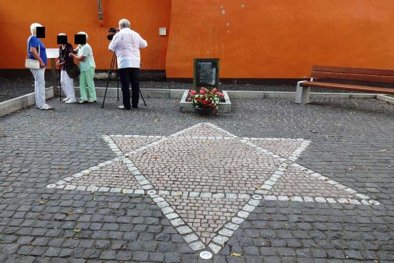 gepflasterter Davidstern mit Lampen im Boden, dahinter der Gedenkstein