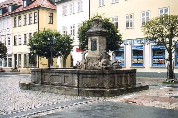 eingefasstes Becken mit einem verzierten Brunnen daran, darauf das Bildnis eines bärtigen Mannes