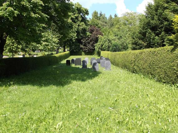 Long drawn lawn, framed on both sides by half-high hedges, in the center several gravestones