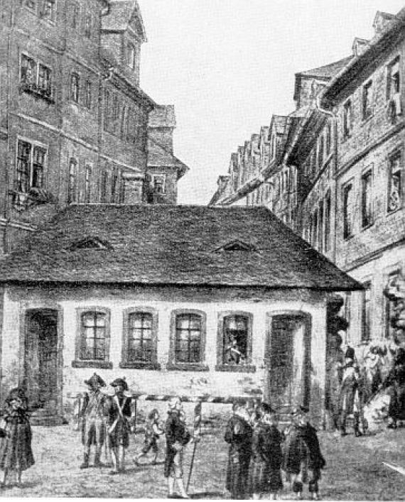 Black and white drawing: small building between high apartment buildings, in front of it several people