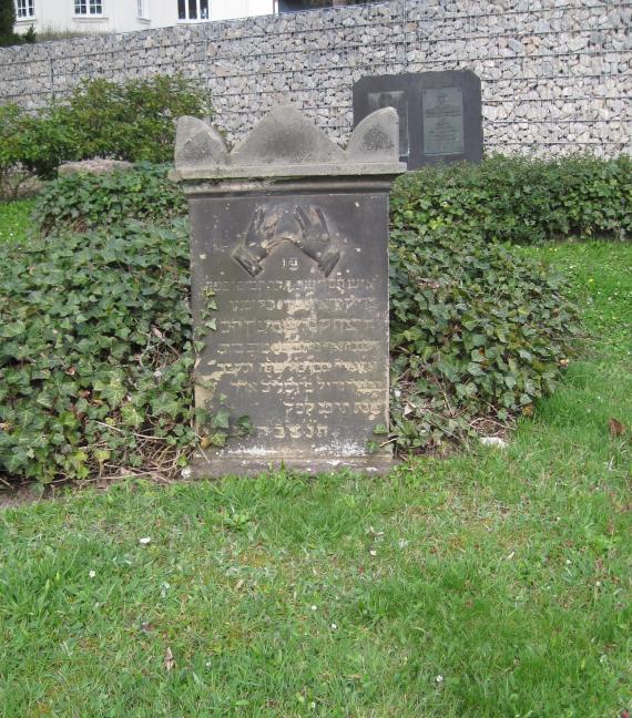 Old tombstone with Hebrew inscription on green lawn