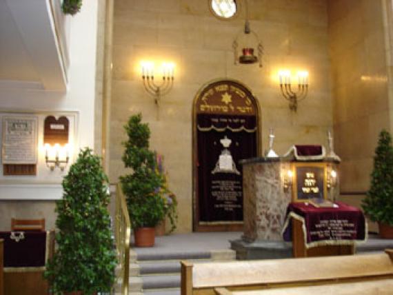 Interior view of synagogue with wooden benches, ornamental trees in yellow light