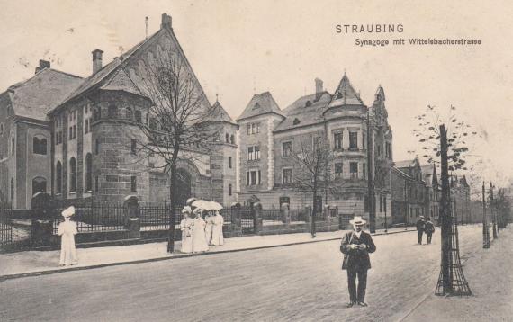 Synagogue with two towers, provided with Stars of David on the top, on the left side of the street of the synagogue along white dressed women walk