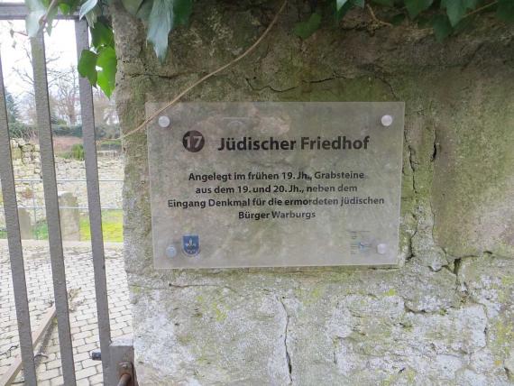 Hinweistafel am Eingang in den Friedhof: "Jüdischer Friedhof. Angelegt im frühen 19. Jh., Grabsteine aus dem 19. und 20. Jh., neben dem Eingang Denkmal für die ermordeten jüdischen Bürger Warburgs". 