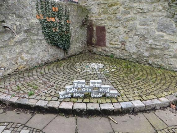 Paved circular floor in with small stones in the center. In front small stones provided with names of the murdered in white writing