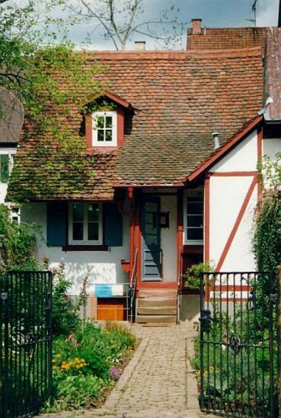 Small house with tiled roof, in front of it a small garden and a black open iron gate