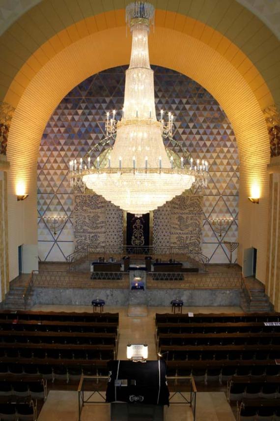 Magnificent interior of a large synagogue, in the center hangs a large chandelier from the ceiling