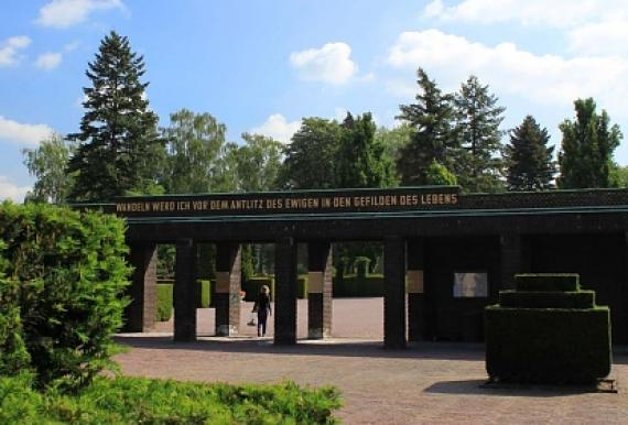 Arkadenmauer auf einem Friedhof, mit Bäumen und Hecken