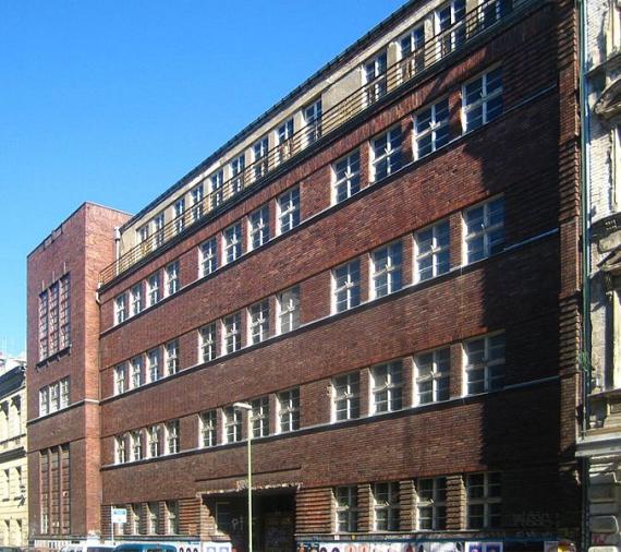 Großes, mehrstöckiges, langes Gebäude aus rotem Backstein. Das Gebäude wurde als Schule genutzt. Es hat viele Fenster.