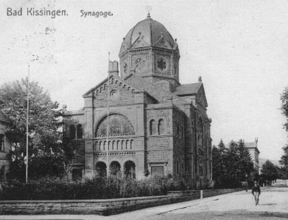 Historical photo of the square in front of the synagogue with fountain on the right, synagogue with dome and decorated facade behind on the left