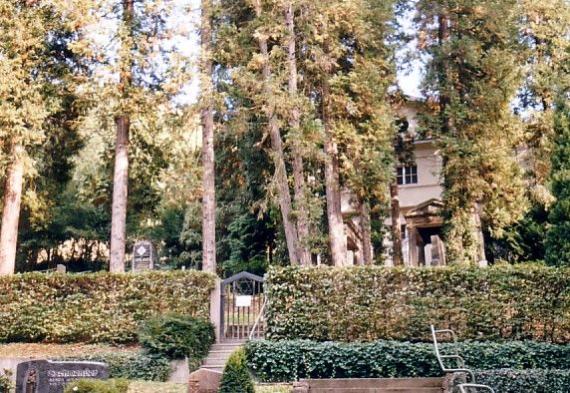 Terrain in the open, with hedges and trees and tombstones, in the background a large house