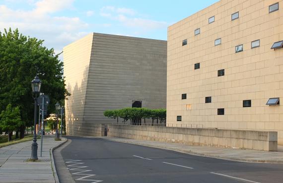 Blick auf eine lange Straße, rechts im Bild zwei große quadratische Gebäude mit kleinen Fenstern
