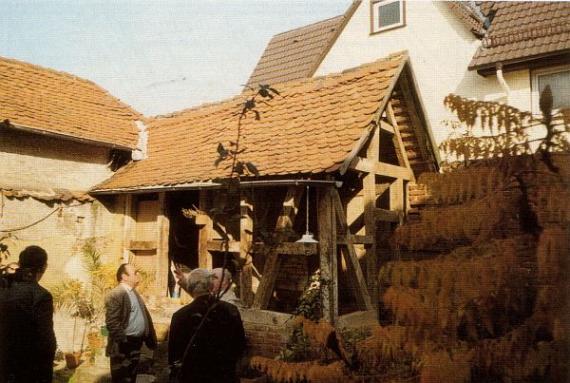 Ein altwirkendes Haus, Außenmauern fehlen, nur Holzbalken zu sehen, bildet den Zugang zur Mikwe