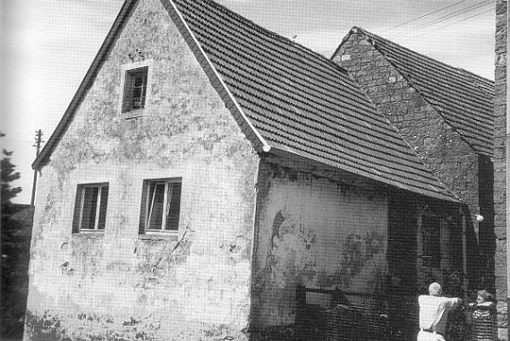 schwarz weiß Bild des kleinen Hauses, das als Synagoge gedient hat. Das Haus ist breit und niedrig und hat drei Fenstern und einem spitzem Dach