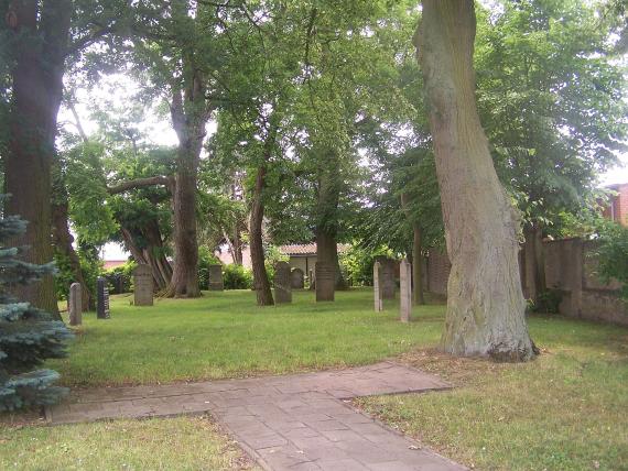 Blick auf grünen Rasen mit einigen Grabsteinen und einen kleinen gepflasterten Weg