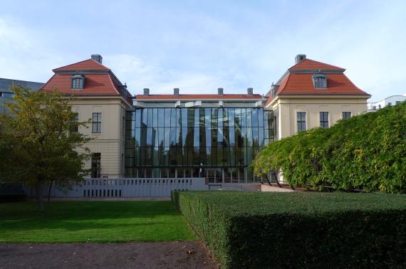 View from the museum garden to a large baroque old building. In its center is a glass cube.