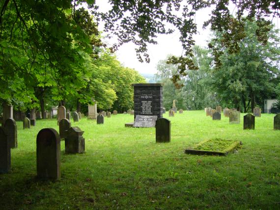 Gravestones scattered on the green lawn, around them trees