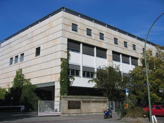 Eckiger, mehrstöckiger Neubau. Links und rechts Bäume. Am Eingang in goldenen Lettern: "Jüdisches Krankenhaus Berlin"