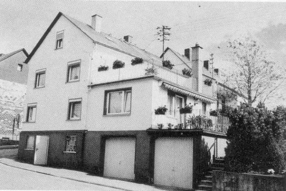 Schwarz-weiß-Aufnahme eines Wohnhauses, Standplatz der ehemaligen Synagoge. Mittlerweile stehen Garagen auf dem Grundstück, wo früher die Gebete stattfanden. Darüber ein Wohnzimmer und weitere Wohnräume, direkt daneben das anschließende Wohnhaus.