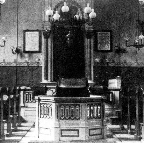 Interior view of the synagogue with wooden benches left and right, in the center a prayer lectern