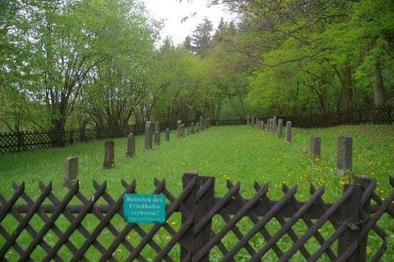 Blick vom hölzernen Eingangstor über den Friedhof, auf einen grünen Rasen 