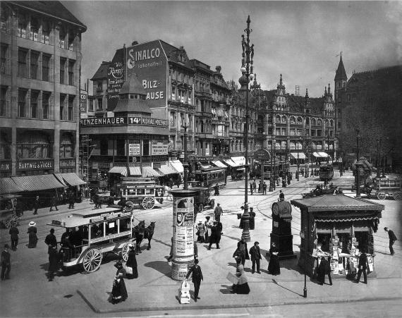 black and white picture of crowded Spittelmarkt in Berlin. A row of bourgeois houses with stores on the left, streetcar and carriages on the right