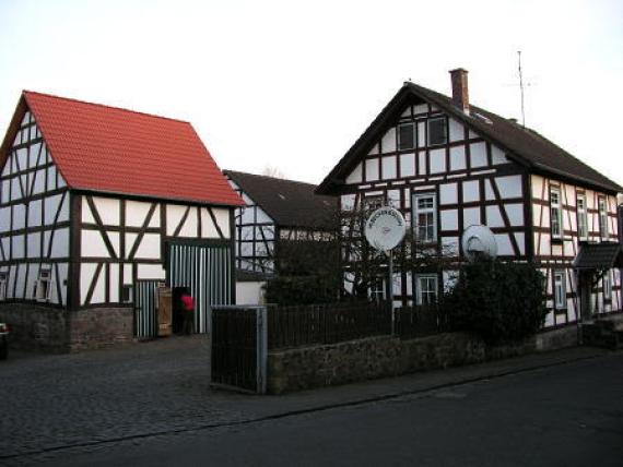 Two half-timbered houses, on the right with light red roof and on the left, the old synagogue building with dark roof. Color photo.