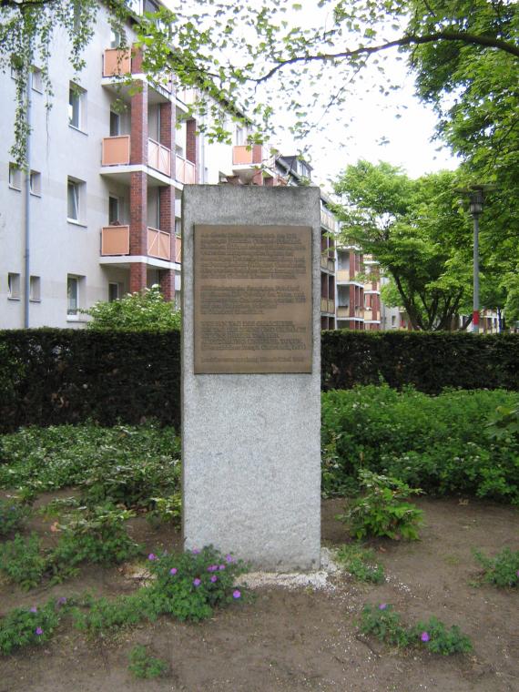 Gedenkstein mit der Geschichte des Friedhofs. Der Gedenkstein liegt mitten im Friedhof, hinten ein Gebäude