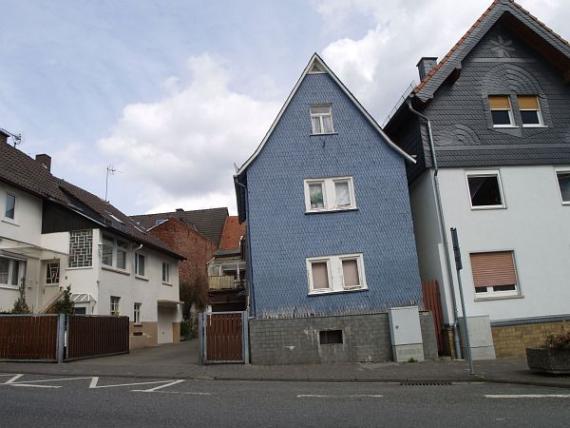 Windschiefe Aufnahme eines kleinen, blauen Hauses mit Satteldach umgeben von Wohnhäusern