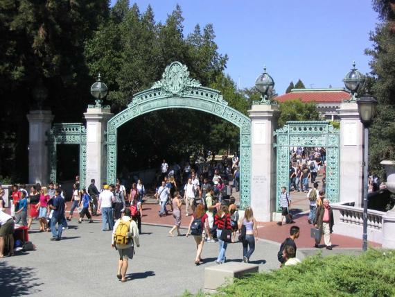 Large gate with two white pillars on the left and right. People go in and out of the university through the gate