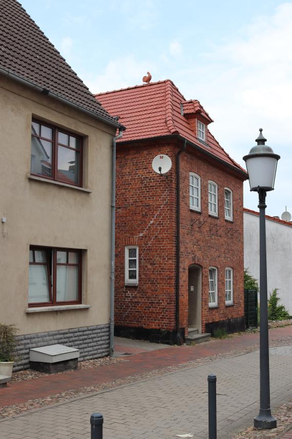 Kleine gepflastere Straße mit Blick auf zwei Häuser, eins davon aus rotem Backstein